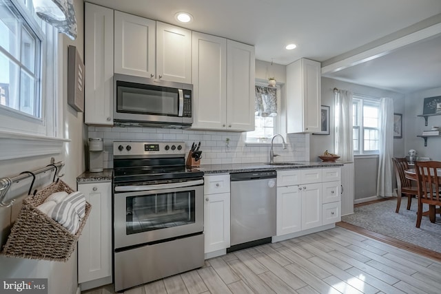 kitchen featuring stainless steel appliances, white cabinetry, sink, and light hardwood / wood-style floors