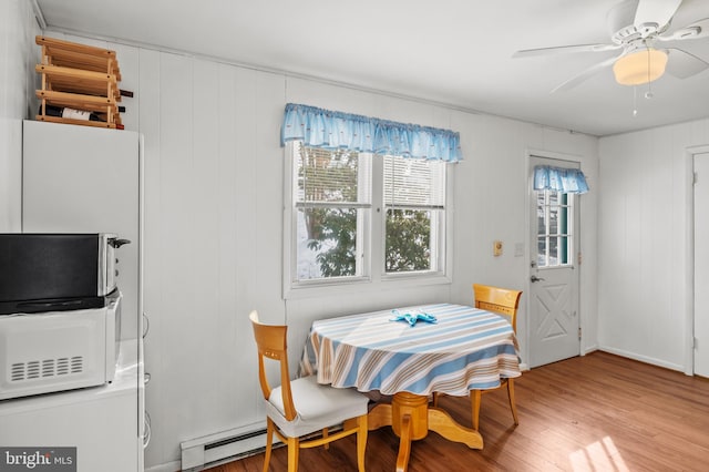 dining area with hardwood / wood-style floors, wooden walls, ceiling fan, and baseboard heating