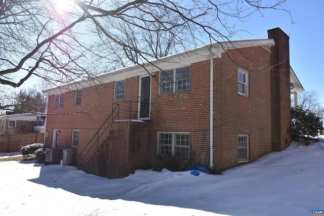 snow covered rear of property featuring central AC unit