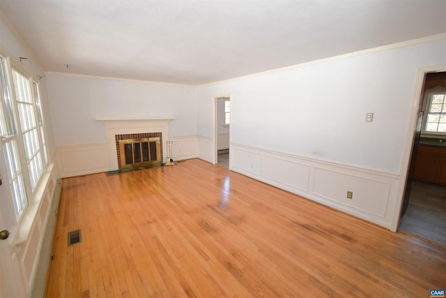 unfurnished living room with light hardwood / wood-style floors, plenty of natural light, ornamental molding, and a fireplace