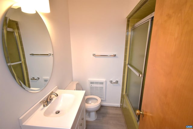 full bathroom featuring toilet, enclosed tub / shower combo, hardwood / wood-style flooring, heating unit, and vanity