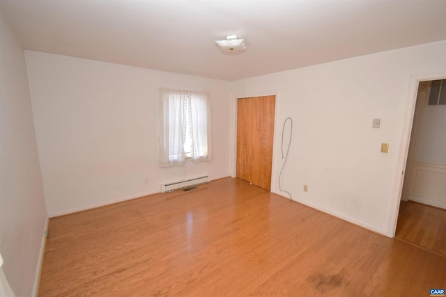 empty room with hardwood / wood-style flooring and a baseboard heating unit