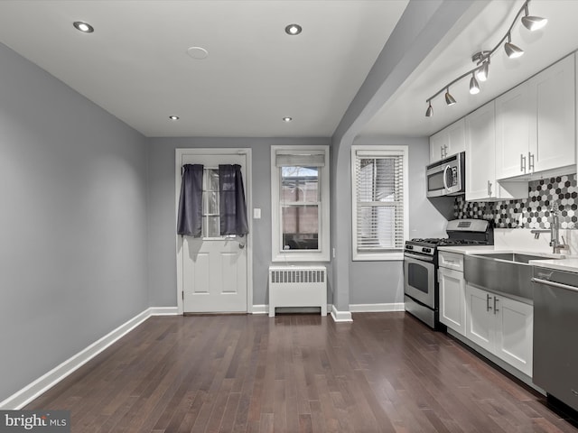 kitchen with dark wood-type flooring, appliances with stainless steel finishes, radiator heating unit, and white cabinets