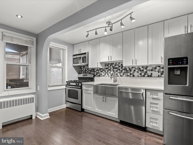 kitchen with radiator, sink, dark wood-type flooring, stainless steel appliances, and white cabinets