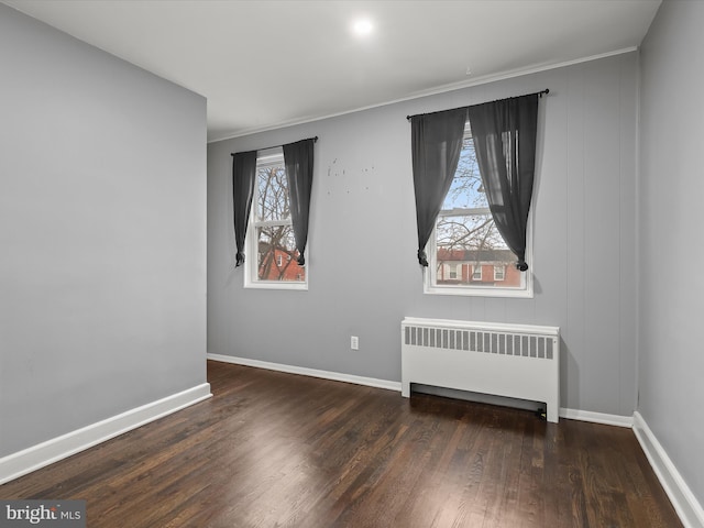 spare room featuring dark wood-type flooring, radiator heating unit, and crown molding