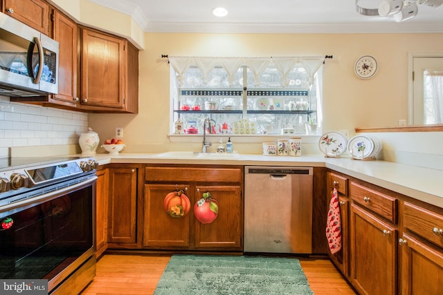 kitchen with sink, backsplash, ornamental molding, stainless steel appliances, and light hardwood / wood-style flooring