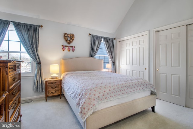 bedroom featuring light carpet, vaulted ceiling, and multiple closets