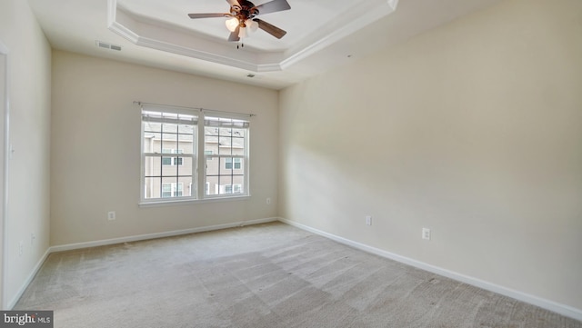 empty room featuring a raised ceiling, light carpet, and ceiling fan