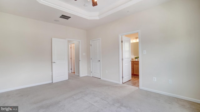 unfurnished bedroom with ensuite bath, light colored carpet, ceiling fan, and a tray ceiling