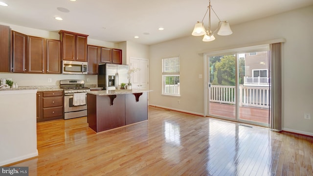 kitchen with a kitchen bar, decorative light fixtures, light hardwood / wood-style flooring, appliances with stainless steel finishes, and a kitchen island