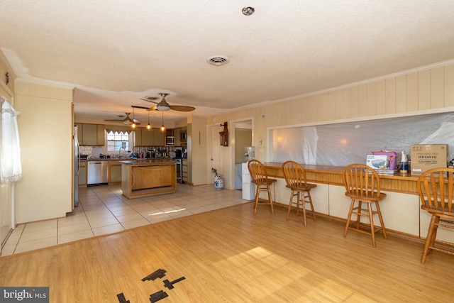 kitchen with a kitchen bar, light wood-type flooring, ornamental molding, ceiling fan, and stainless steel appliances