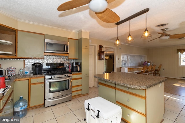 kitchen with light tile patterned floors, ceiling fan, stainless steel appliances, a center island, and ornamental molding