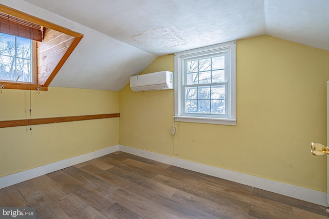 bonus room featuring lofted ceiling, a wall mounted air conditioner, hardwood / wood-style floors, and a textured ceiling