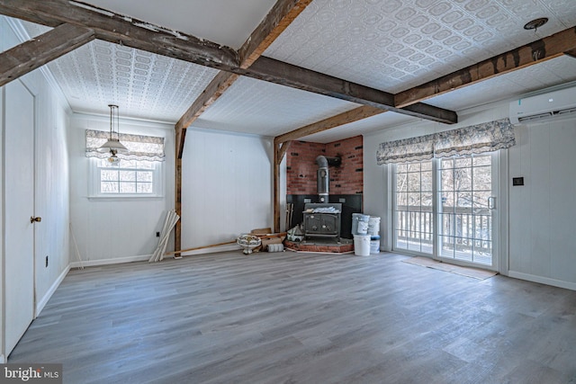 unfurnished living room featuring hardwood / wood-style floors, a wall mounted air conditioner, a healthy amount of sunlight, and a wood stove