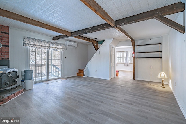 unfurnished living room with beam ceiling, a wood stove, hardwood / wood-style floors, and a wall unit AC