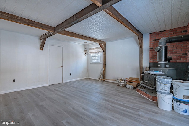 unfurnished living room featuring beam ceiling, light hardwood / wood-style floors, and a wood stove