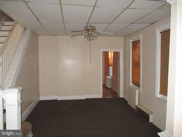 spare room with radiator heating unit, dark colored carpet, ceiling fan, and a paneled ceiling