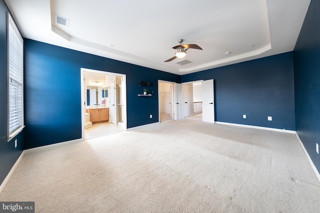 unfurnished bedroom featuring a tray ceiling, carpet, visible vents, and baseboards