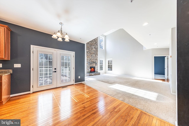 interior space with light wood-type flooring, a notable chandelier, a stone fireplace, and french doors