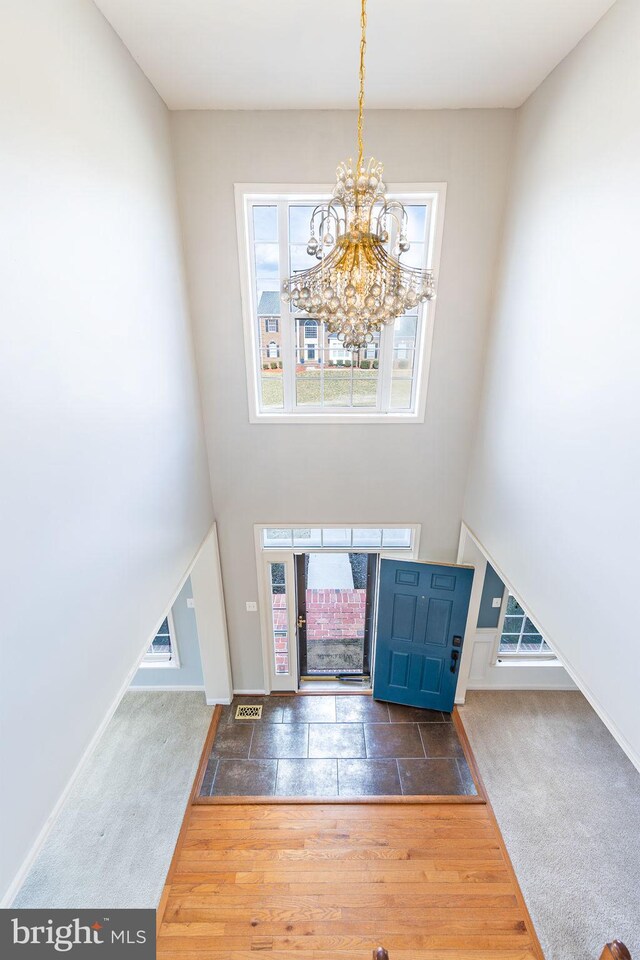 carpeted entrance foyer featuring a chandelier, a high ceiling, wood finished floors, and visible vents