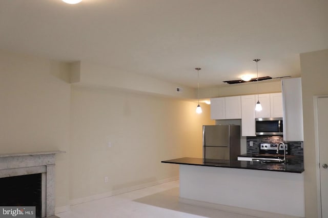 kitchen featuring pendant lighting, appliances with stainless steel finishes, white cabinetry, a premium fireplace, and decorative backsplash