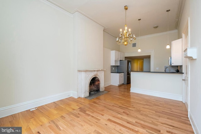 unfurnished living room featuring sink, light hardwood / wood-style floors, an inviting chandelier, and ornamental molding