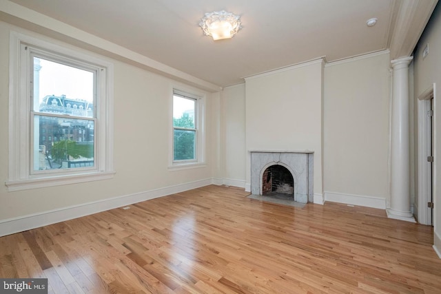 unfurnished living room featuring light wood-type flooring, a brick fireplace, ornate columns, and crown molding