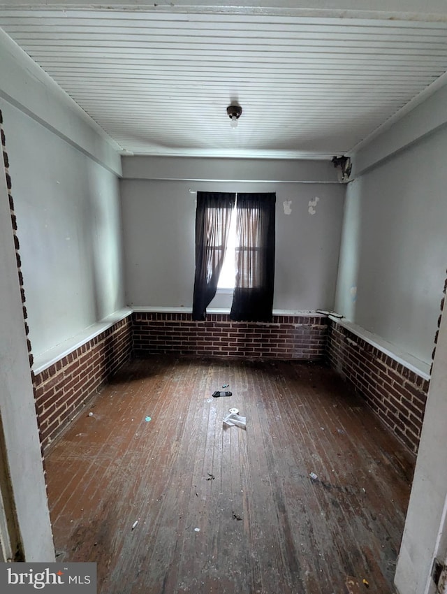 unfurnished room with hardwood / wood-style flooring and brick wall