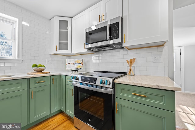 kitchen with white cabinetry, green cabinetry, decorative backsplash, stainless steel appliances, and light stone counters