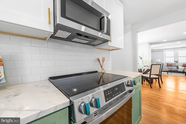 kitchen with white cabinets, appliances with stainless steel finishes, decorative backsplash, green cabinets, and light hardwood / wood-style flooring