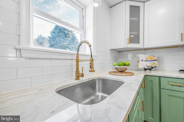 interior details featuring light stone counters, sink, white cabinets, and green cabinetry