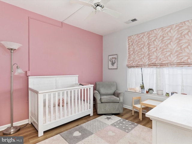 bedroom with a nursery area, ceiling fan, and wood-type flooring