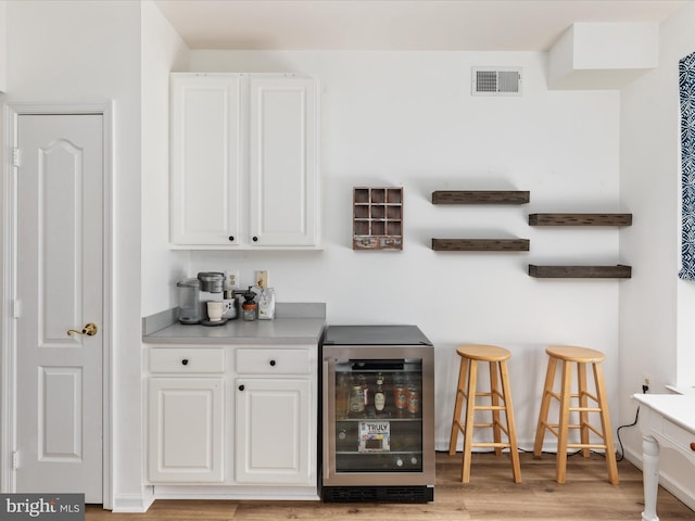 bar with white cabinetry, beverage cooler, and light hardwood / wood-style floors