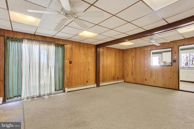 unfurnished room with a baseboard heating unit, wooden walls, light colored carpet, and ceiling fan