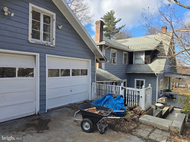 view of side of home with a deck, a garage, roof with shingles, and a chimney