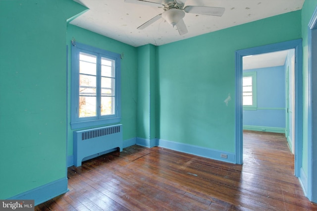 spare room featuring hardwood / wood-style floors, radiator, baseboards, and plenty of natural light