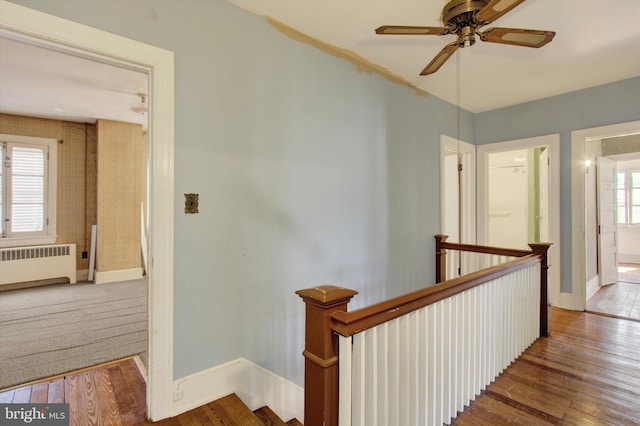 corridor with an upstairs landing, radiator, and wood finished floors