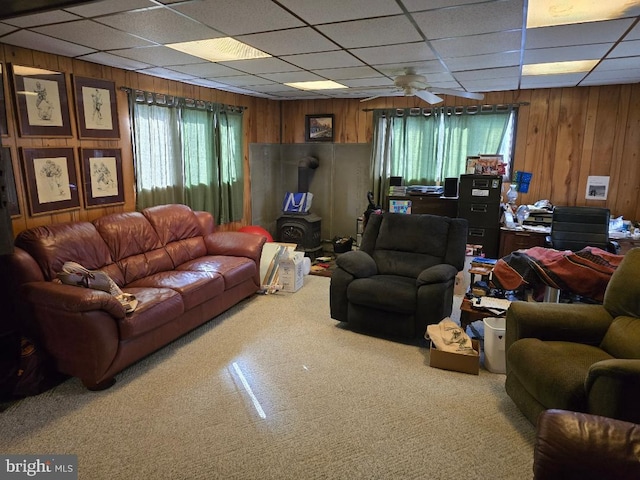 living room with a drop ceiling, wooden walls, and ceiling fan