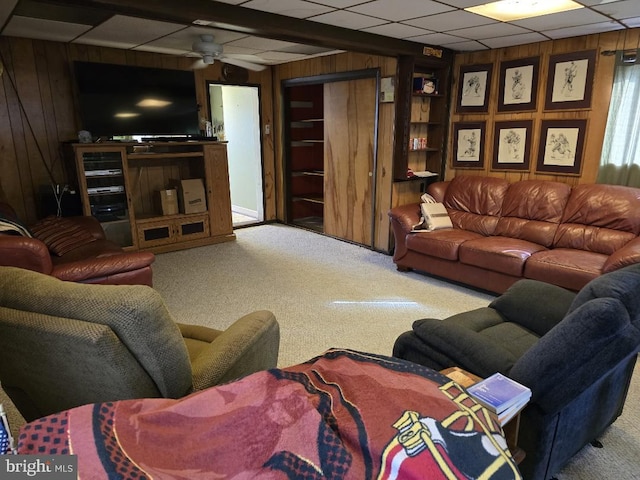 living room with a drop ceiling, carpet floors, wooden walls, and ceiling fan