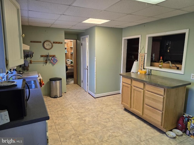 kitchen featuring dark countertops, a paneled ceiling, baseboards, and a sink