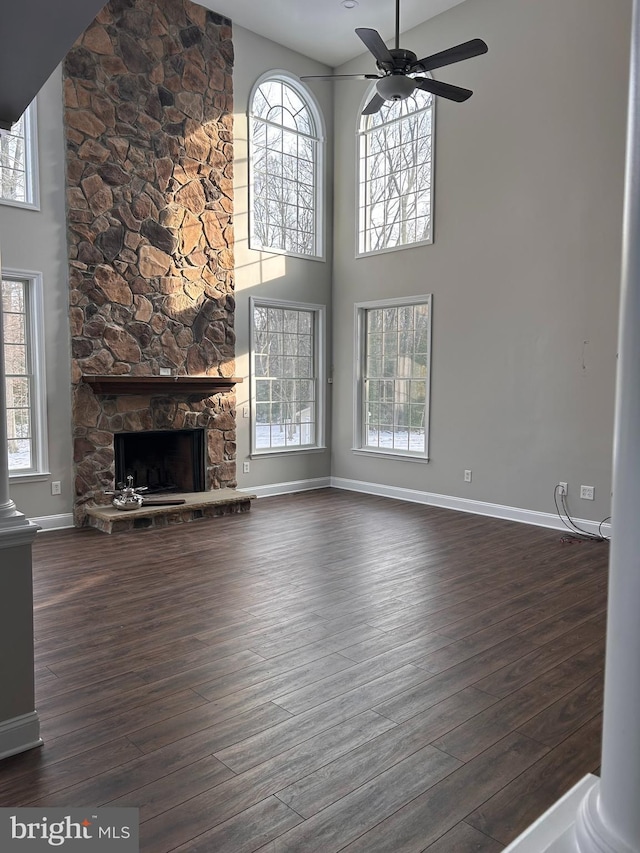 unfurnished living room with dark wood-type flooring, ceiling fan, a fireplace, and a towering ceiling