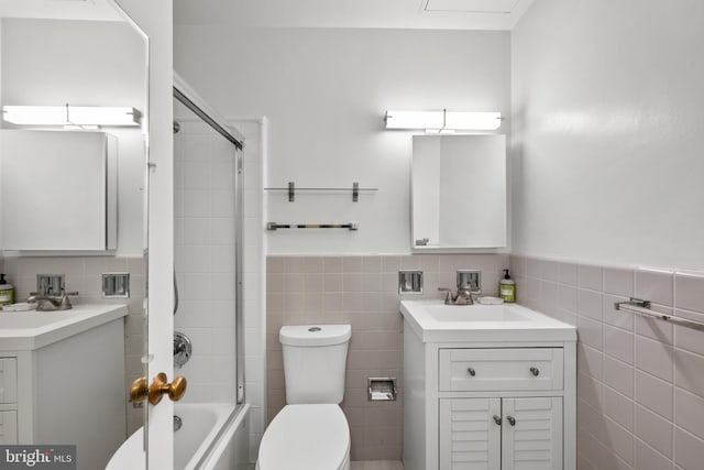 full bathroom featuring vanity, toilet, tile walls, and combined bath / shower with glass door