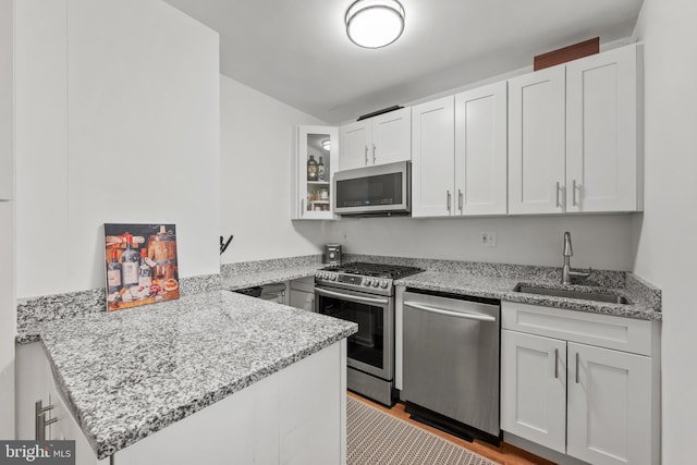 kitchen featuring sink, white cabinets, kitchen peninsula, stainless steel appliances, and light stone countertops