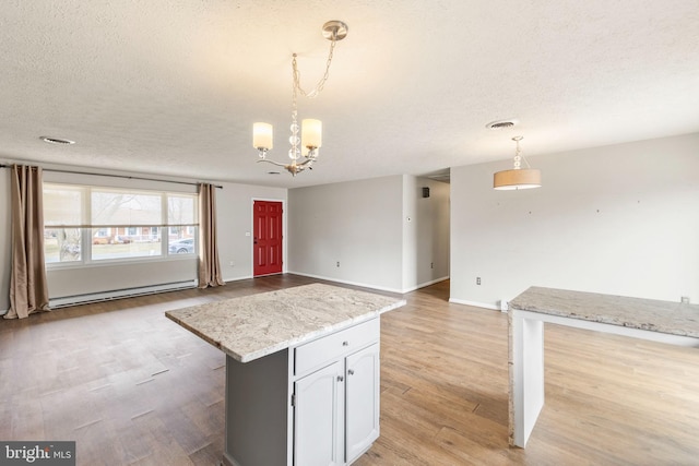 kitchen with visible vents, light wood-style flooring, decorative light fixtures, a textured ceiling, and a baseboard heating unit