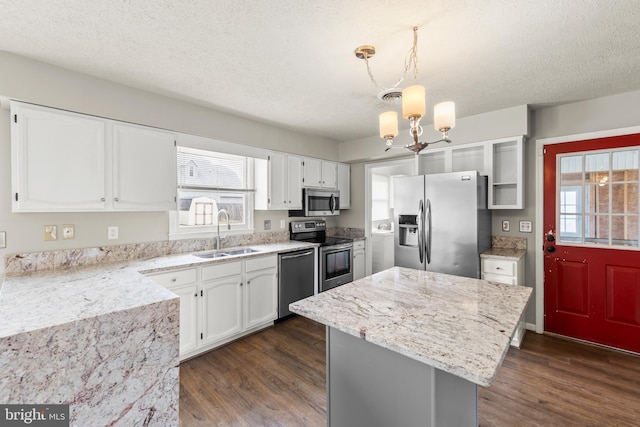 kitchen with white cabinets, a kitchen island, stainless steel appliances, pendant lighting, and a sink