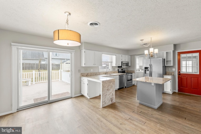 kitchen featuring a kitchen island, white cabinetry, stainless steel appliances, and decorative light fixtures