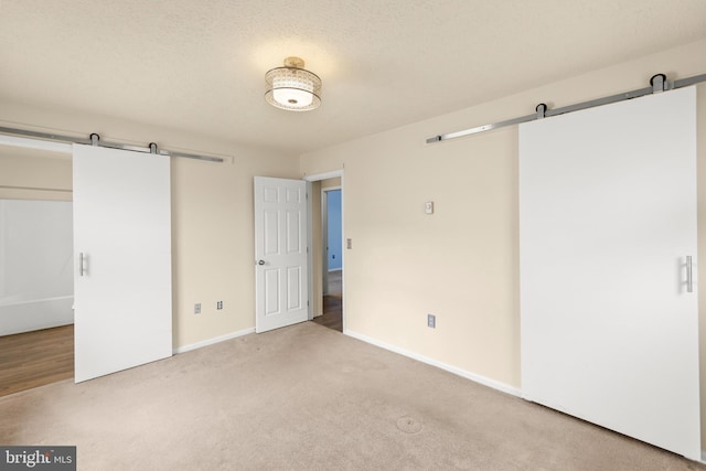 unfurnished bedroom with carpet flooring, a textured ceiling, baseboards, and a barn door