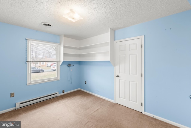 spare room featuring a baseboard heating unit, light carpet, and visible vents