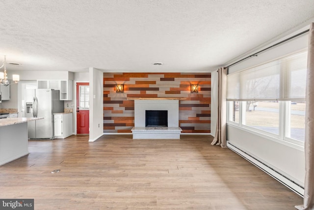 unfurnished living room featuring a fireplace with raised hearth, a textured ceiling, a chandelier, a baseboard heating unit, and light wood-type flooring