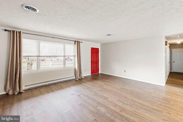 empty room with baseboards, visible vents, baseboard heating, and wood finished floors